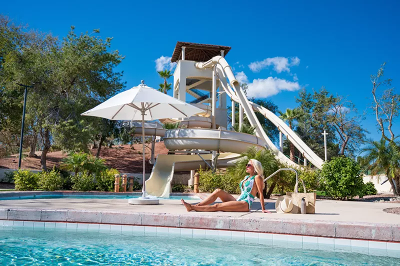 Image: A woman sitting by a pool with a waterslide in the background.