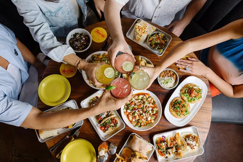 Image: Clinking drinks over a table filled with plates of food.