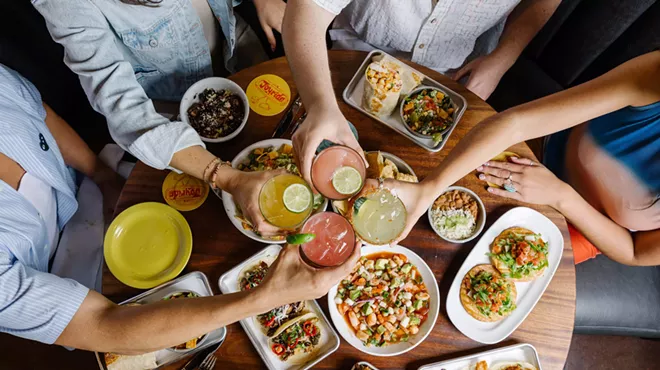 Clinking drinks over a table filled with plates of food.