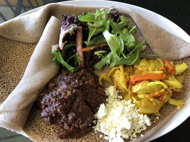 Image: Stewed chicken, house-made cheese, cabbage, and greens on injera.