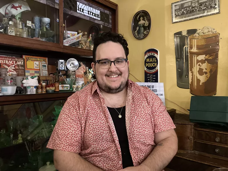 Image: a man with black hair and glasses smiles