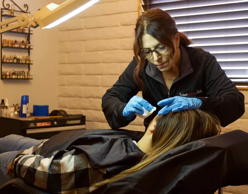 Image: A woman removes a tattoo off of another woman.