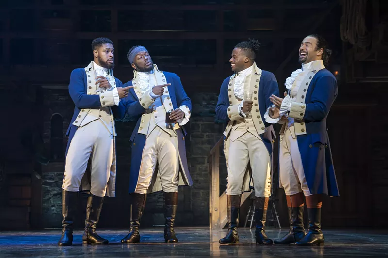 Image: Four men dressed in old-fashioned clothes standing together on a stage.
