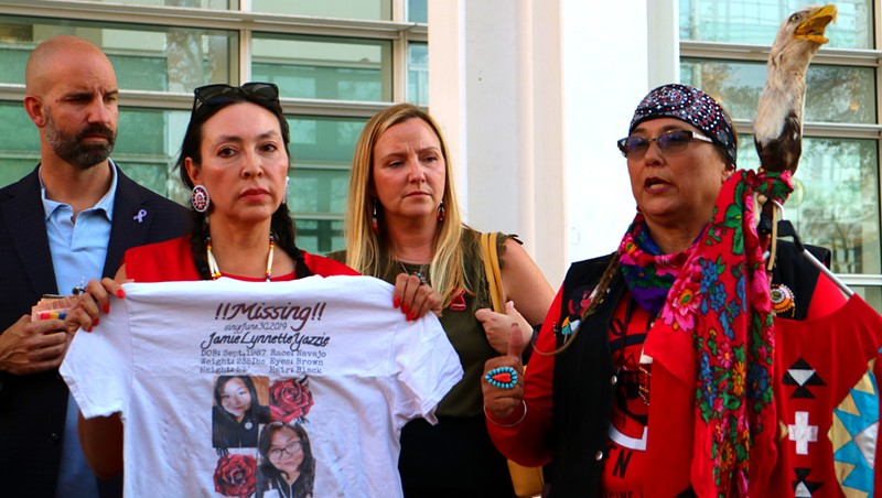 Attorney Darlene Gomez holds up a Jamie Yazzie t-shirt while Luvy Yonnie addresses a crowd outside Sandra Day O'Connor U.S. Courthouse. Jim Schmidt and Tara Petito, the stepparents of murder victim Gabby Petito, stand behind them.