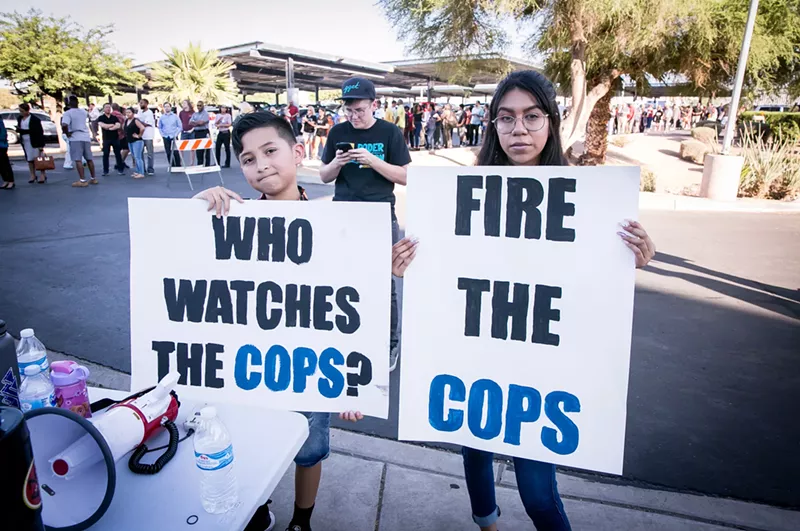 Image: protesters with signs that say "Who watches the cops?" and "fire the cops"