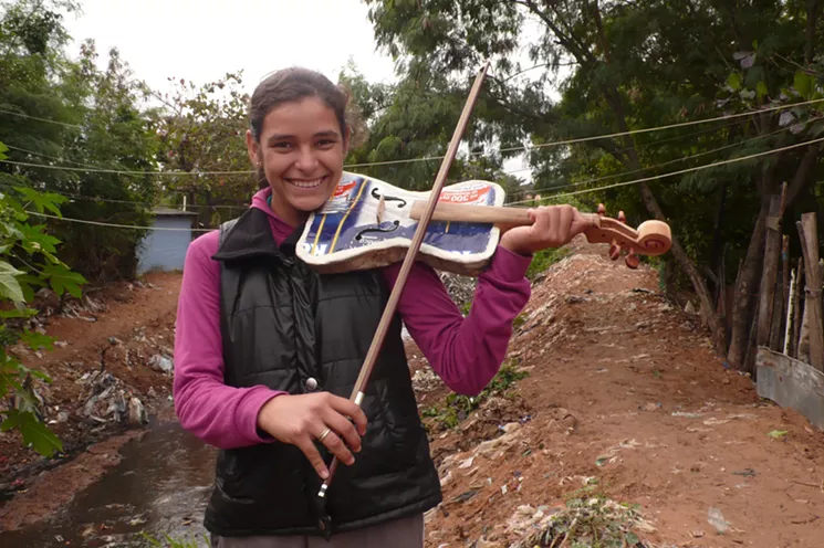 A young musician plays a violin made out of discarded objects in Landfill Harmonic. - LANDFILL HARMONIC