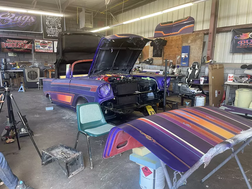 An old car with the hood up in a workshop.