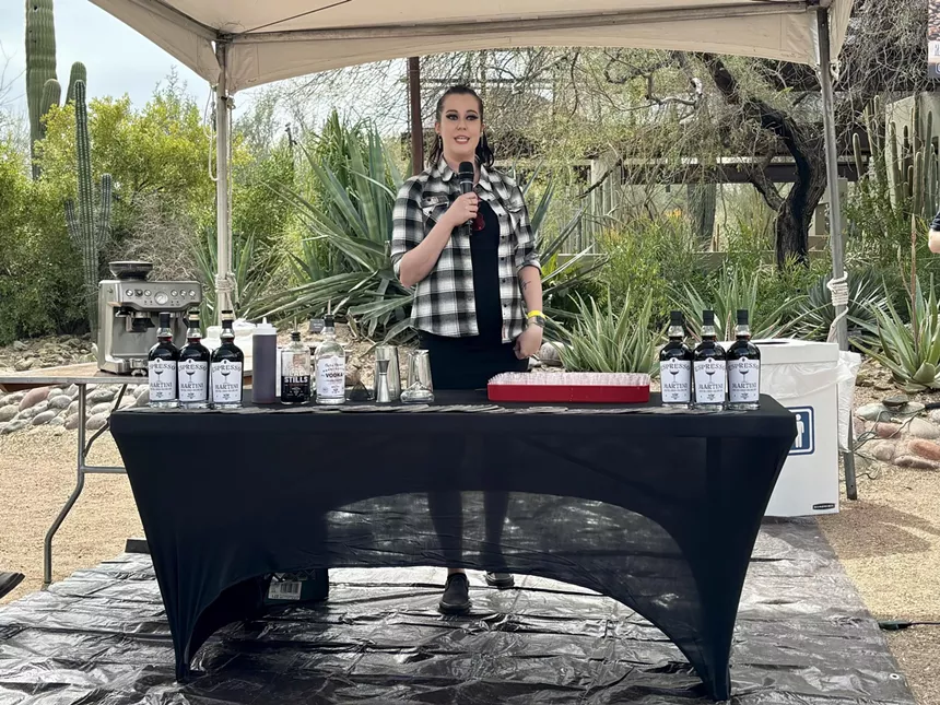 Bartender displays bottles in front of a desert backdrop.