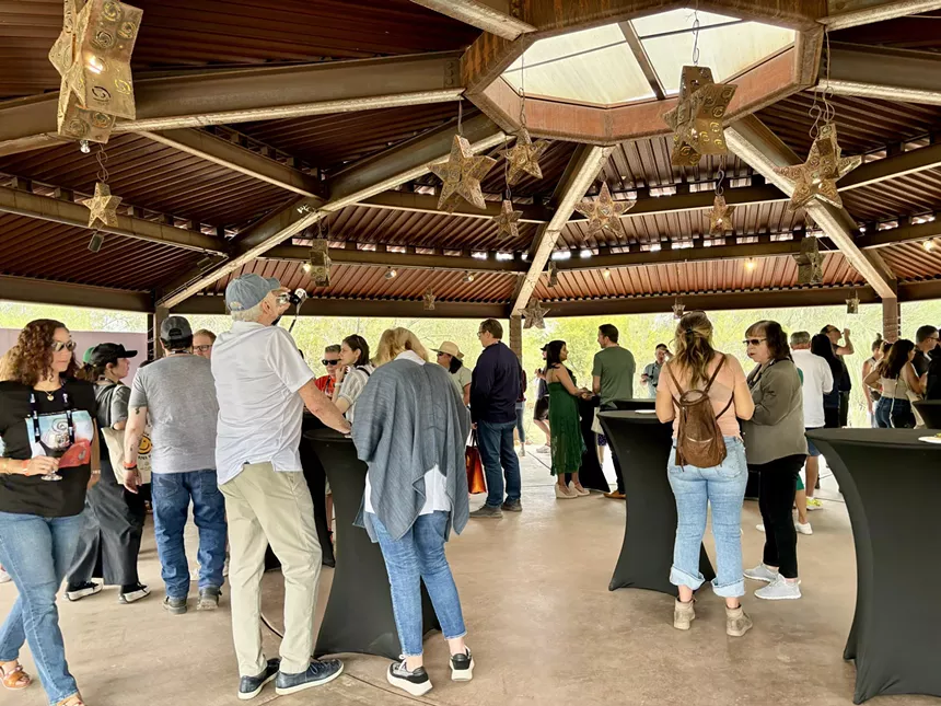 People stand at tables under a pavilion.