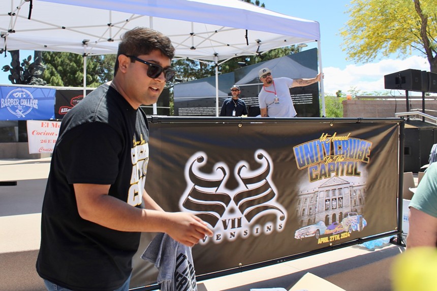 A man in sunglasses holds a t-shirt in front of a DJ booth.