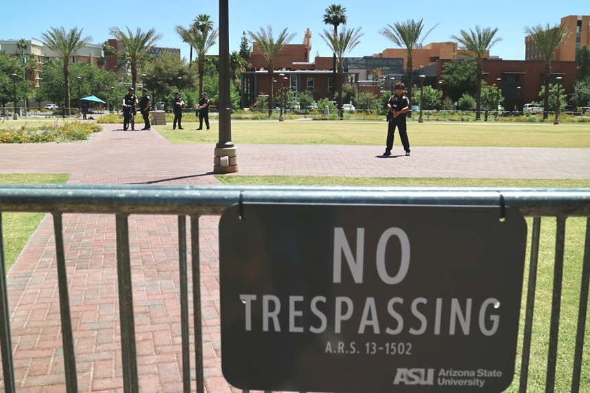 A 'no trespassing sign' in the foreground and five police officers standing in the background.