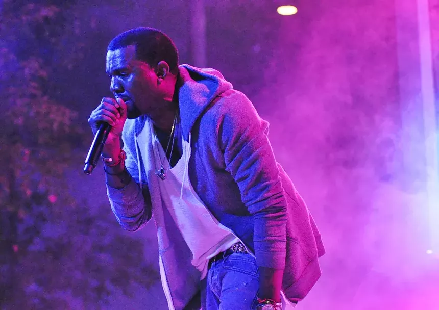Kanye West on stage holding a microphone.