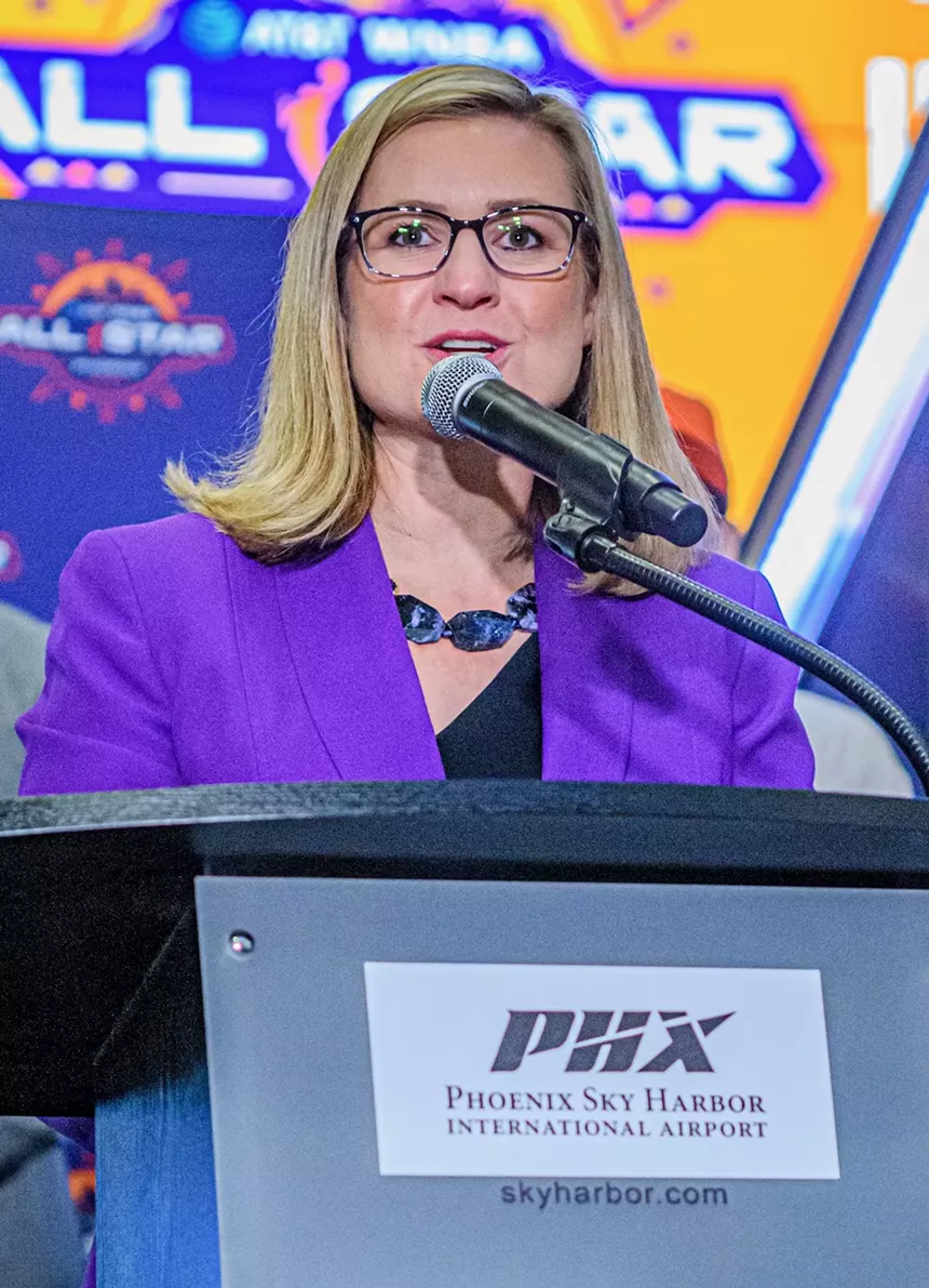 A woman in a purple blazer speaks at a podium