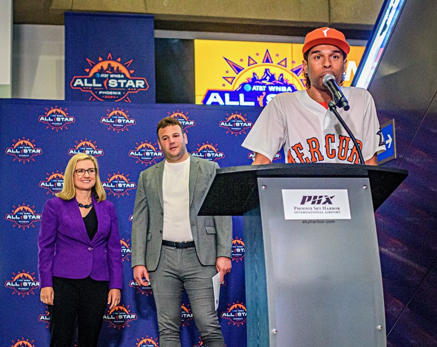 A man in an orange cap and white Mercury baseball-style shirt speaks at a podium