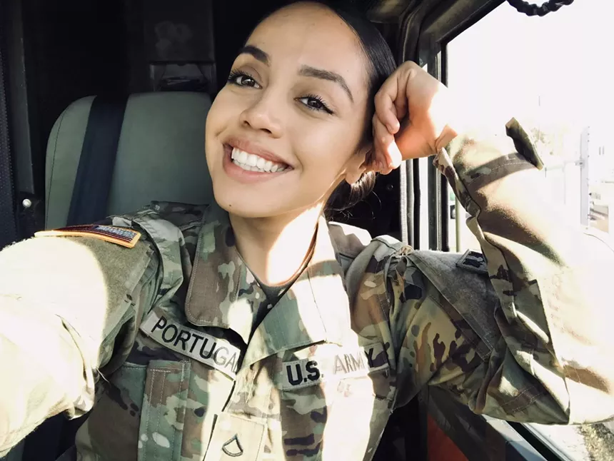 A woman in combat fatigues poses for a selfie in a car.
