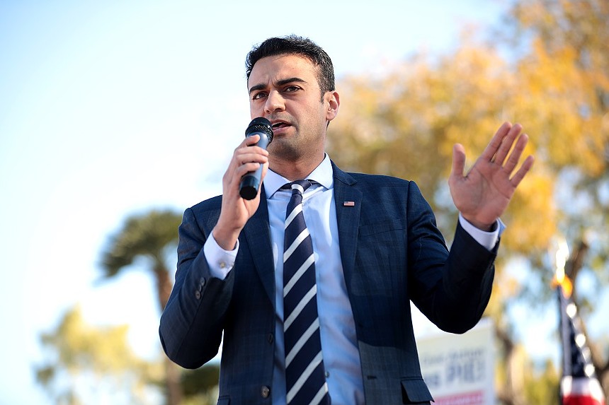 A man in a suit and tie speaking into a microphone outdoors