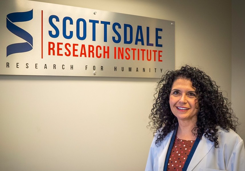 a woman in a lab coat stnads in front of a sign for Scottsdale Research Institute