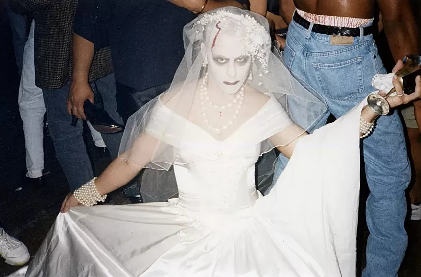 A man with a painted face wearing a white wedding dress.