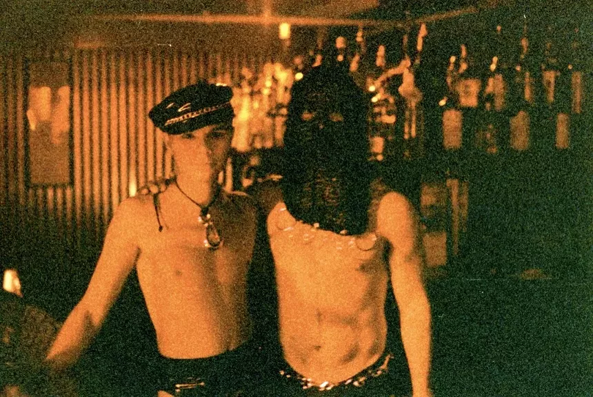 Two shirtless men standing in a nightclub.