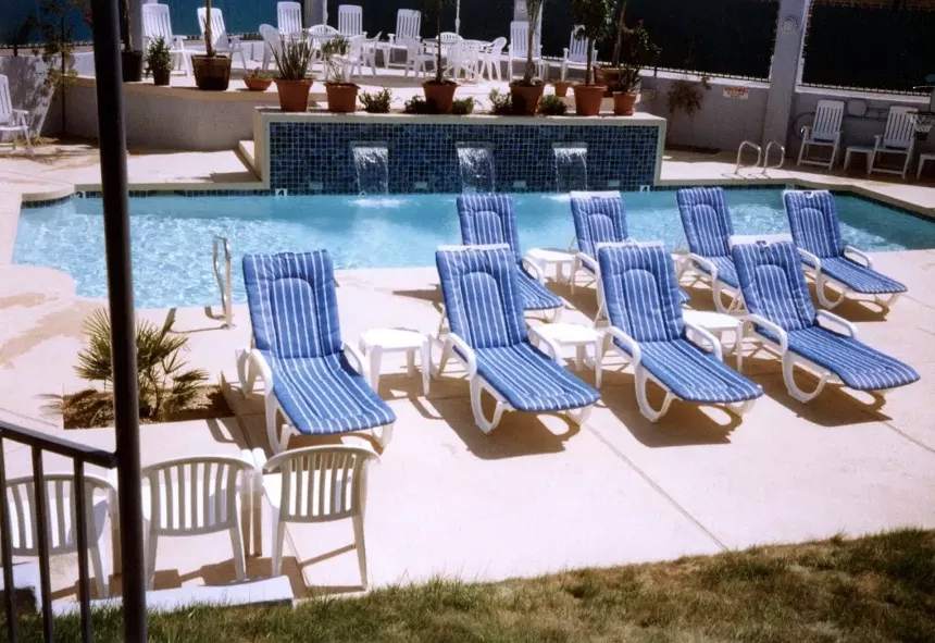 A group of chaise lounge chairs next to an outdoor swimming pool.
