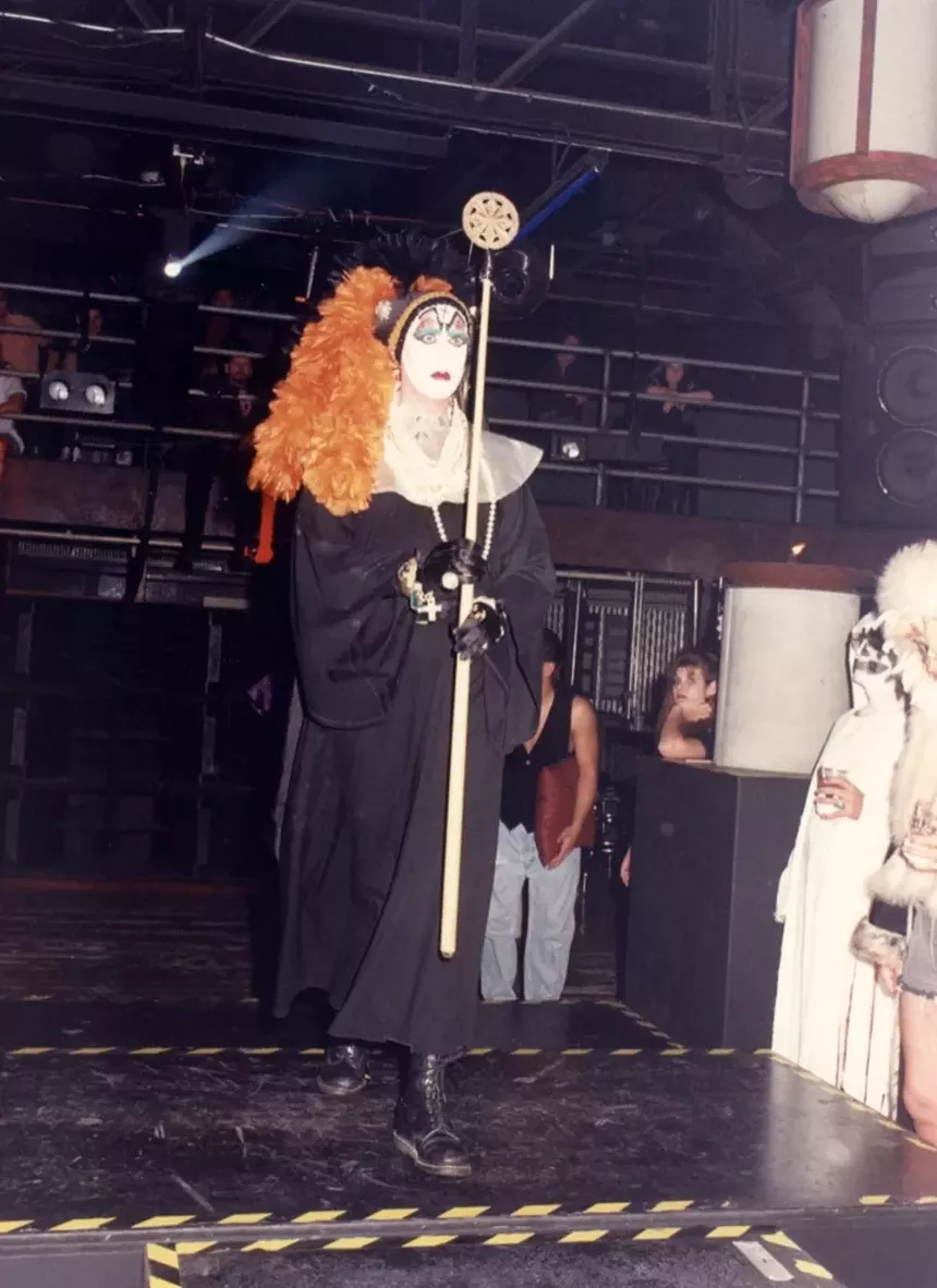 A drag queen walks down a catwalk inside a nightclub.