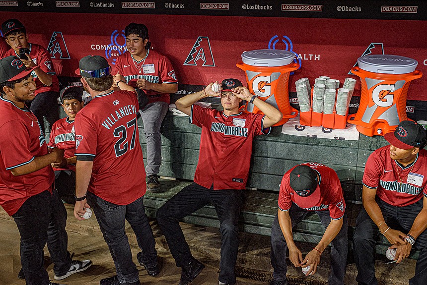Boys in red jerseys sit in a baseball dugout