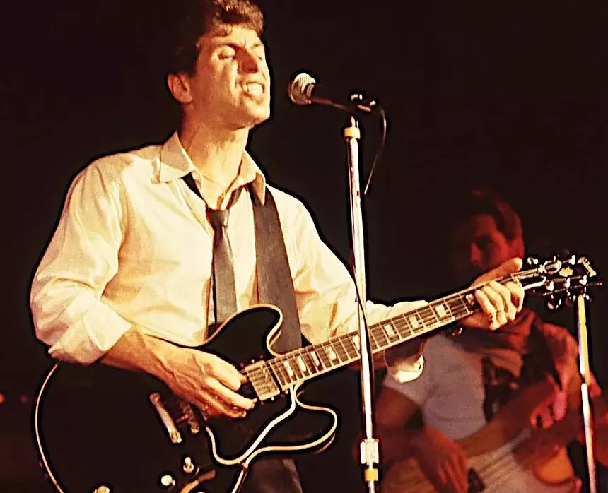 A male rock guitarist performing onstage.