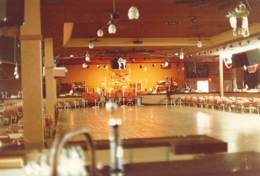 A large dance floor and stage in a cavernous room inside a nightclub.