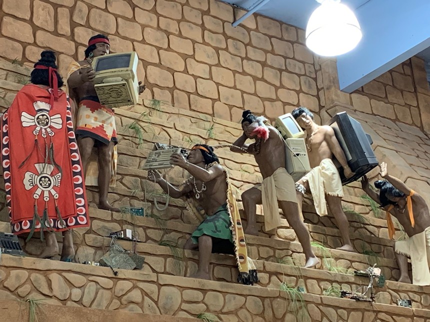 A display of mannequins that look like ancient Aztecs carrying pieces of modern technology.