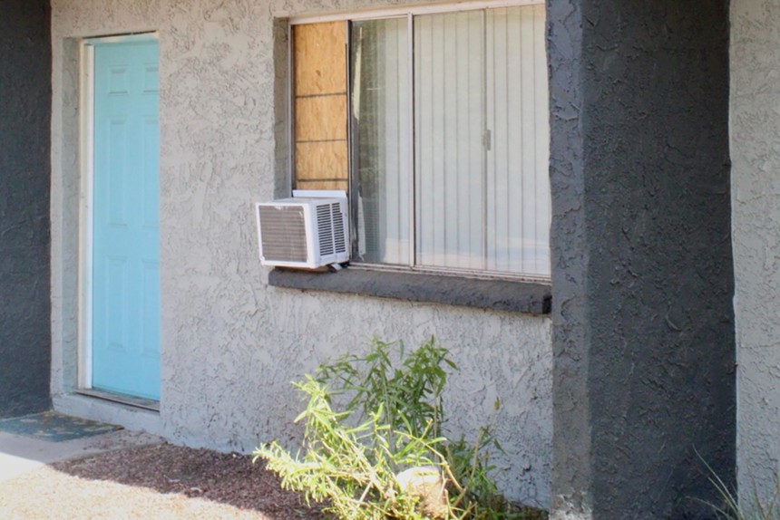 A window air conditioning unit hangs out of a boarded-up window