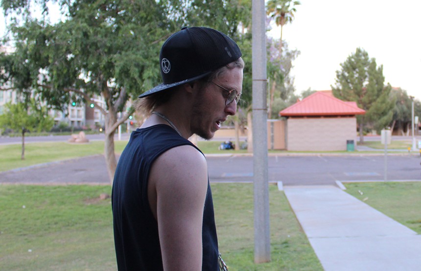 A man in glasses, a backward black hat and a black tank top looks at the ground