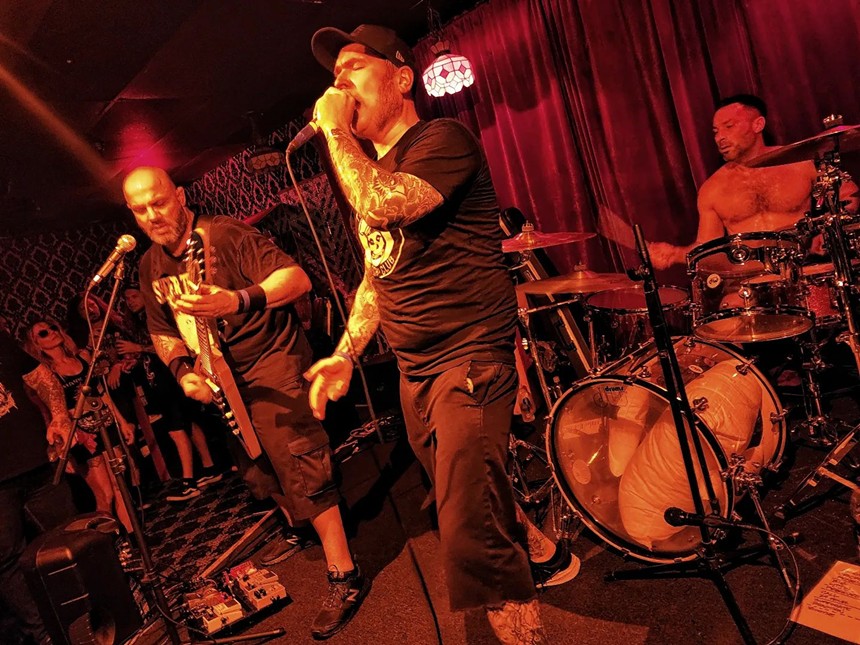 A rock band performs on a stage inside a bar drenched in red light.