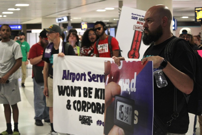 Workers stand in Phoenix Sky Harbor International Airport's Terminal 4 baggage claim with signs demanding heat protections.