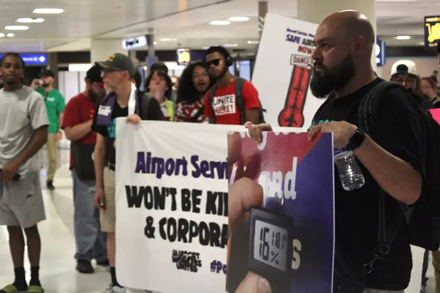 Workers stand in Phoenix Sky Harbor International Airport's Terminal 4 baggage claim with signs demanding heat protections.