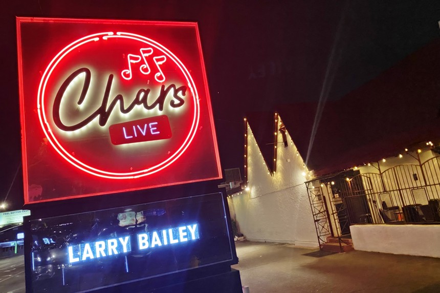 A neon sign and the exterior of a bar at night.