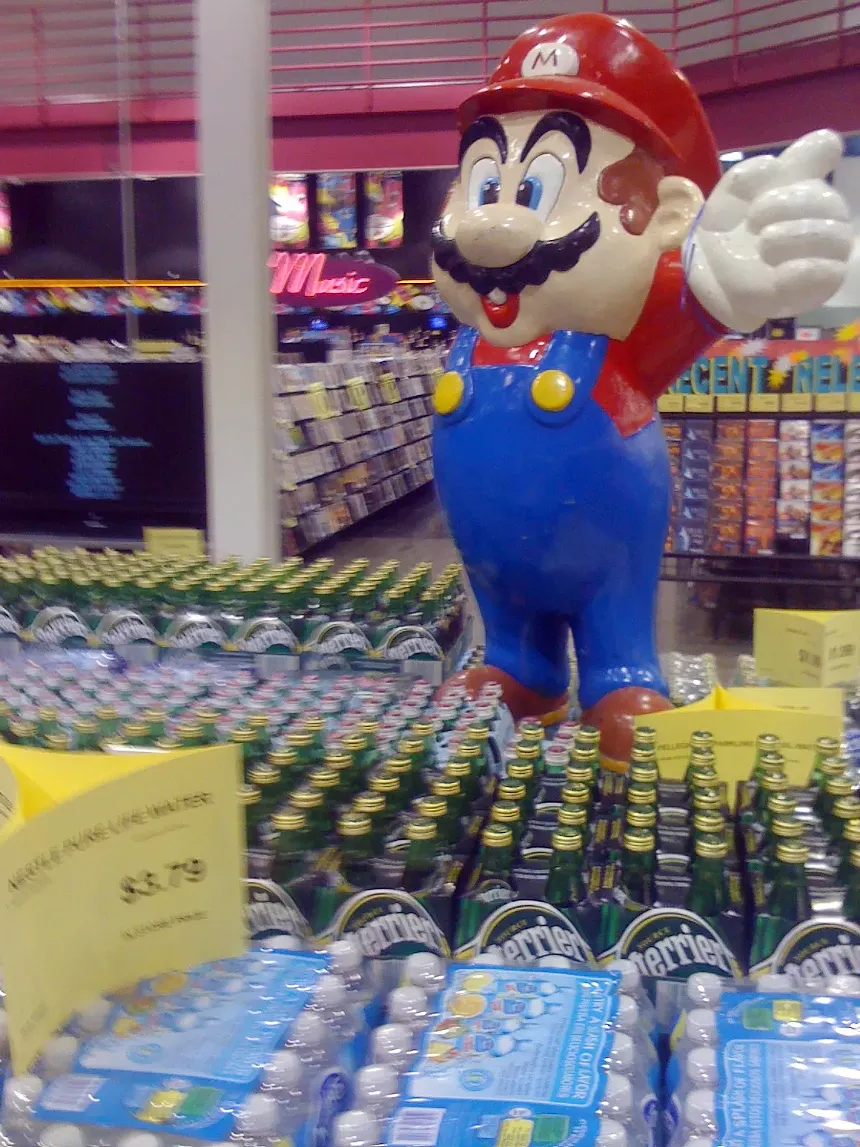 A statue of the Nintendo character Mario in the middle of bottles of water for sale at a store.