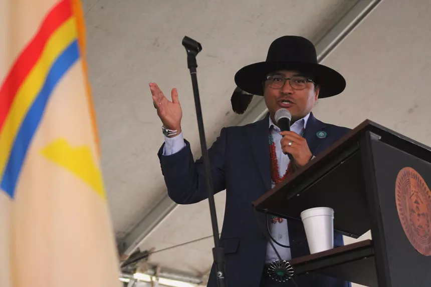 A man in a hat speaks into a microphone while his other hand is open.