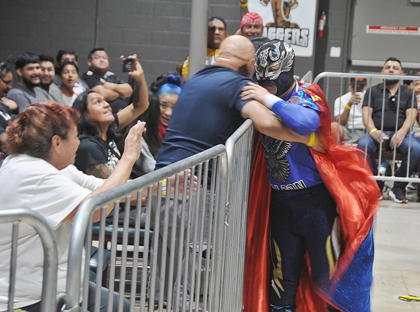 A masked professional wrestler hugs a fan.