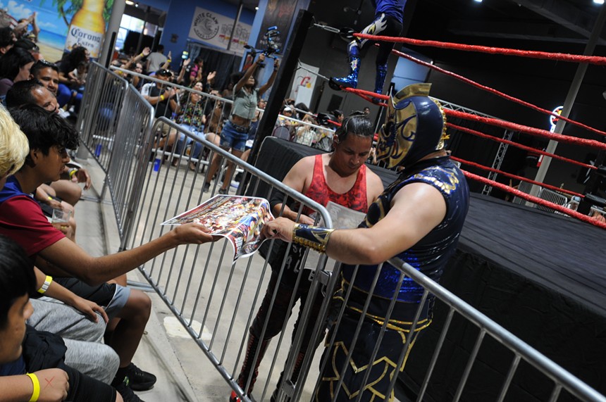 Professional wrestlers sign fans' posters at ringside.