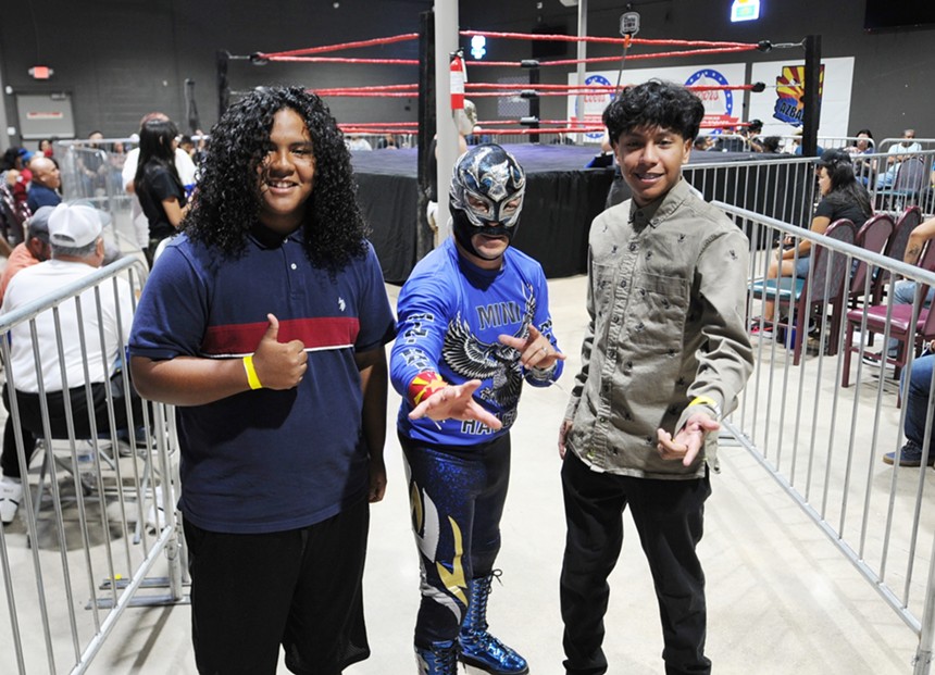 Wrestling fans pose for a photo with a masked wrestler.