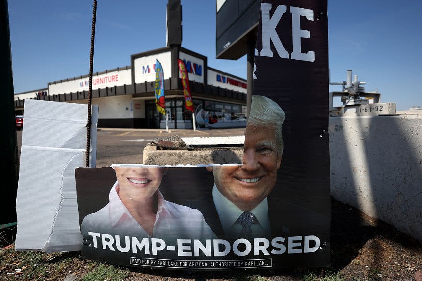 a torn campaign sign for Donald Trump and Kari Lake