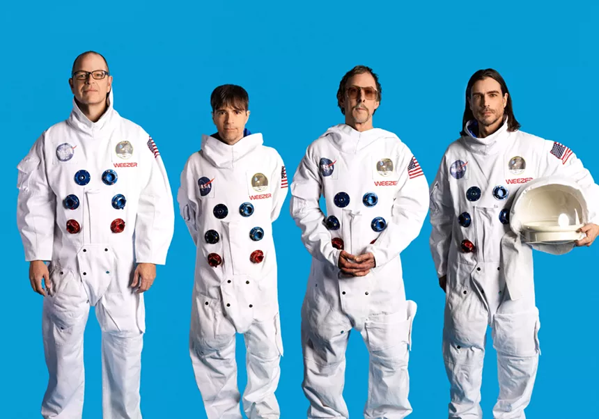 Four men in space suits in front of a blue background.