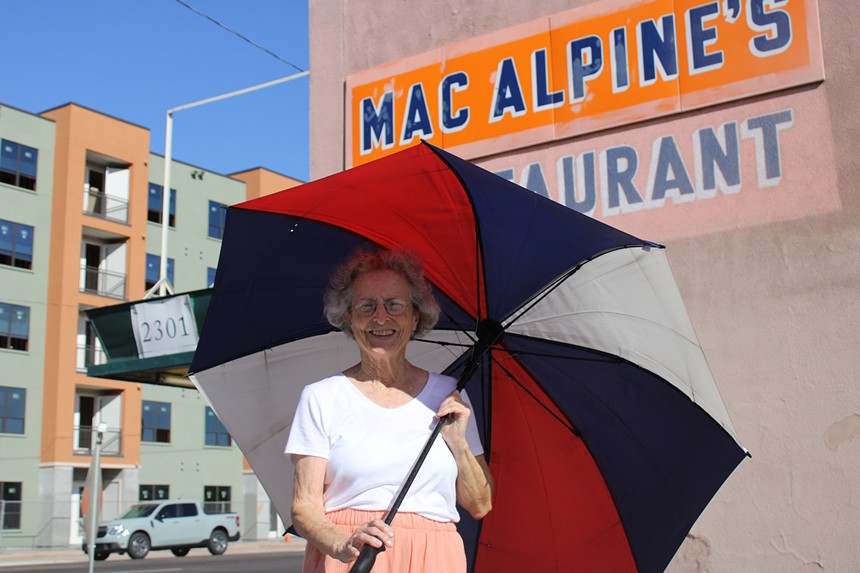 a elderly woman in front of MacAlpine's Diner with a red, orange and blue umbrella