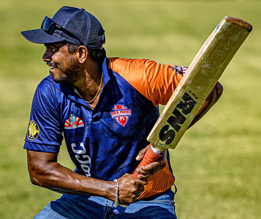 a man in an orange and blue shirt readies to swing a cricket bat