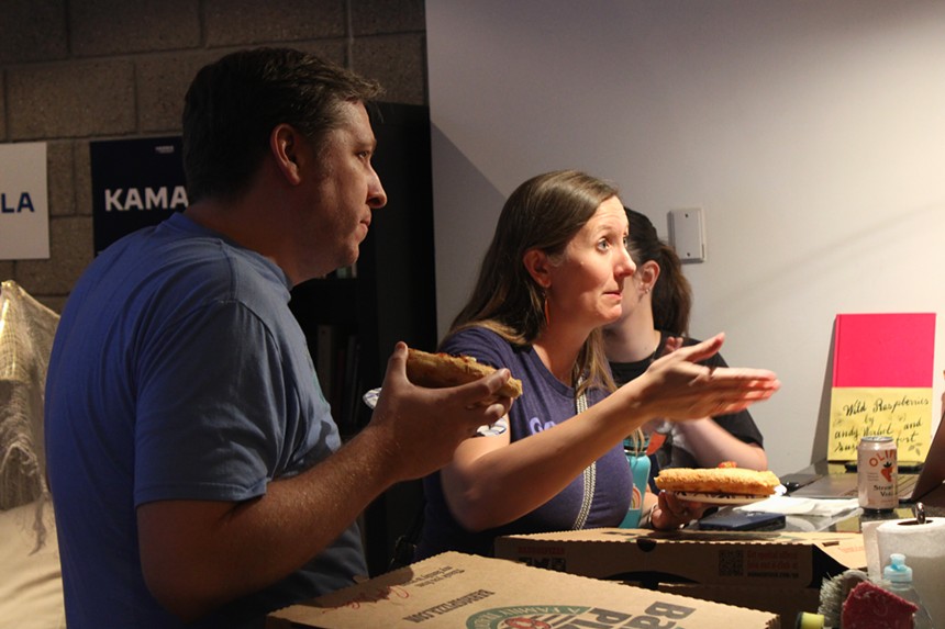 a woman and man stand at a counter, the woman gestures and talks