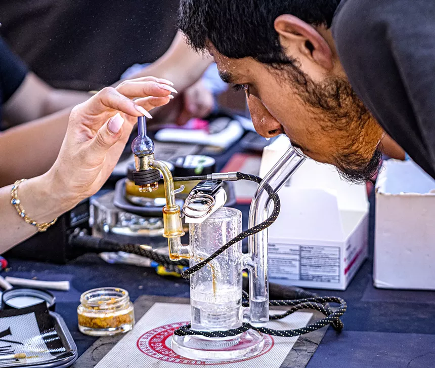 A man takes a hit from a dab rig as a bead of sweat collects on his nose.