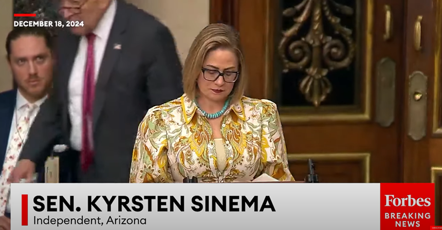 chuck schumer walks behind kyrsten sinema during a speech
