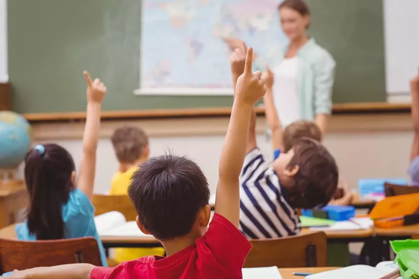 elementary school students raise their hands in a classroom