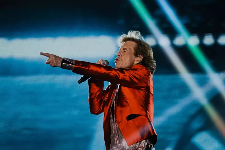 A long-haired man points while singing into a microphone.