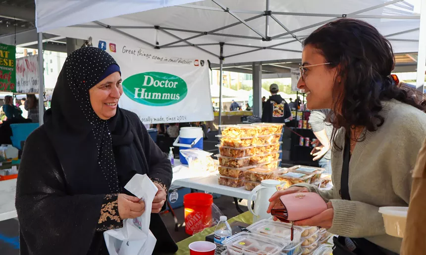 a woman selling syrian food chats with a customer at a farmer's market